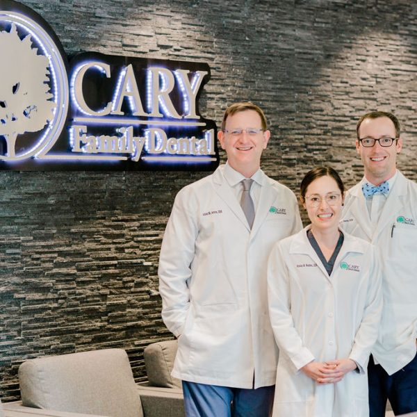 The dentists at Cary Family Dental in Cary, NC, standing in front of their practice sign