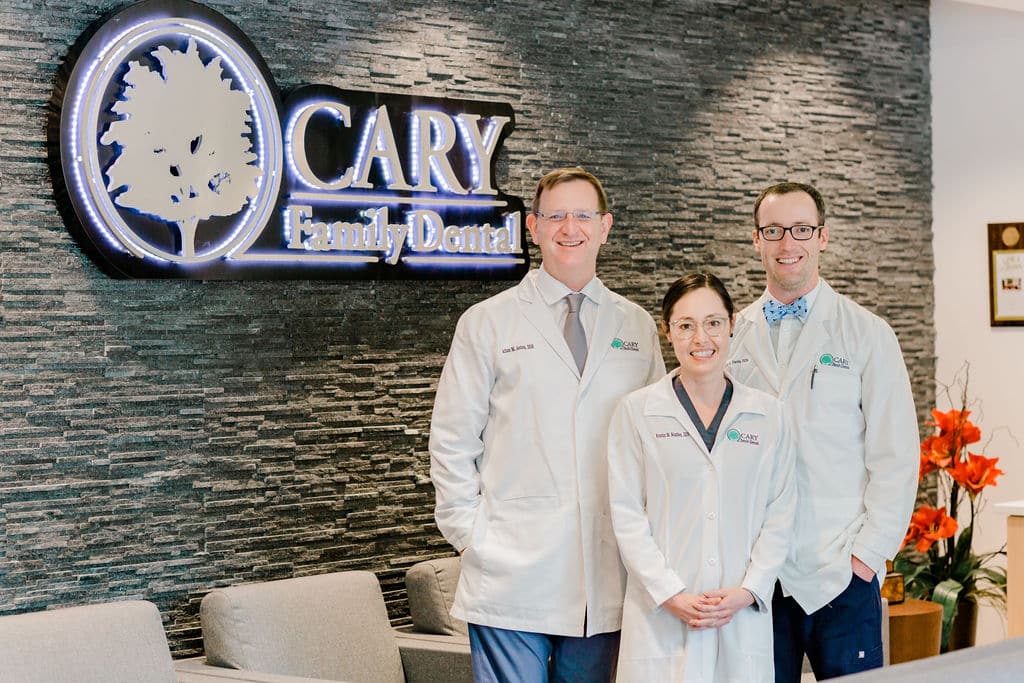 The dentists at Cary Family Dental in Cary, NC, standing in front of their practice sign