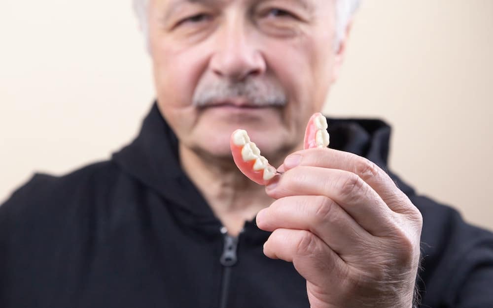 A man holds up some traditional dentures